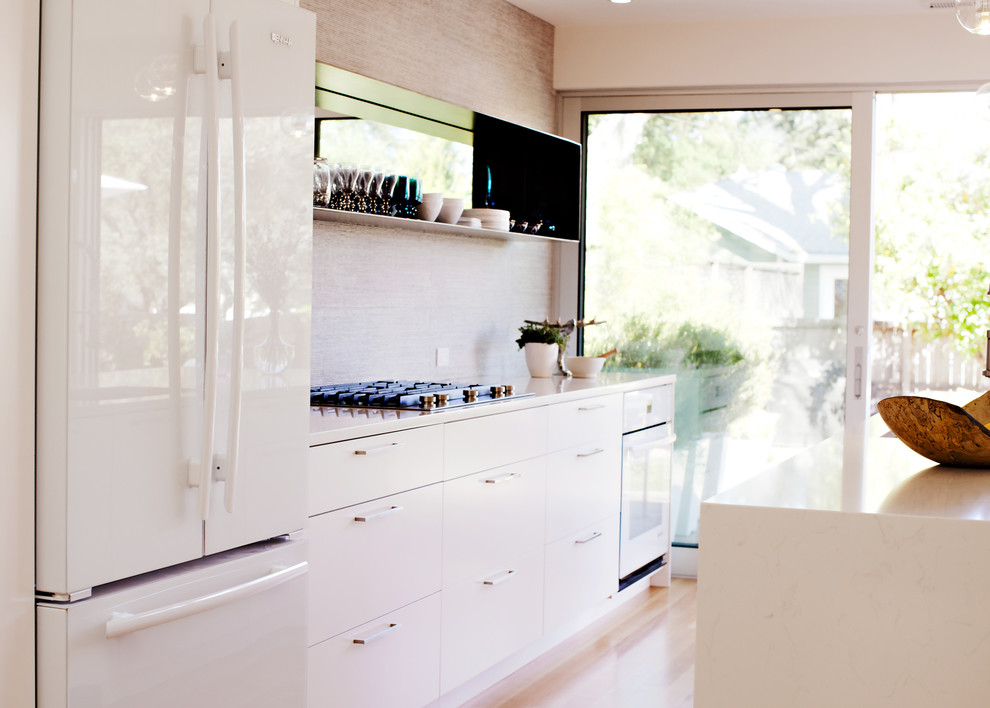Cette photo montre une petite cuisine américaine parallèle moderne avec parquet clair, un évier encastré, un placard à porte plane, des portes de placard blanches, un plan de travail en quartz modifié, une crédence grise, une crédence en carreau de porcelaine, un électroménager blanc et îlot.