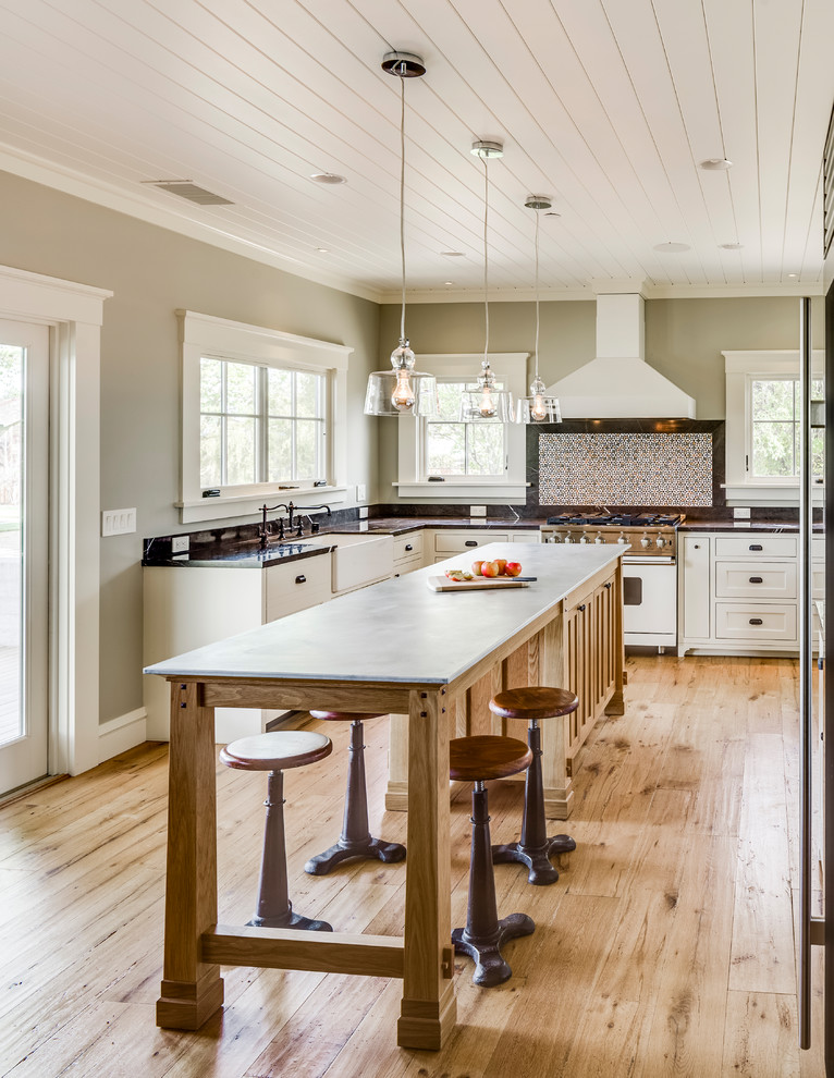 Example of a mid-sized transitional u-shaped light wood floor and beige floor eat-in kitchen design in San Francisco with a farmhouse sink, recessed-panel cabinets, white cabinets, marble countertops, black backsplash, marble backsplash, white appliances, an island and black countertops
