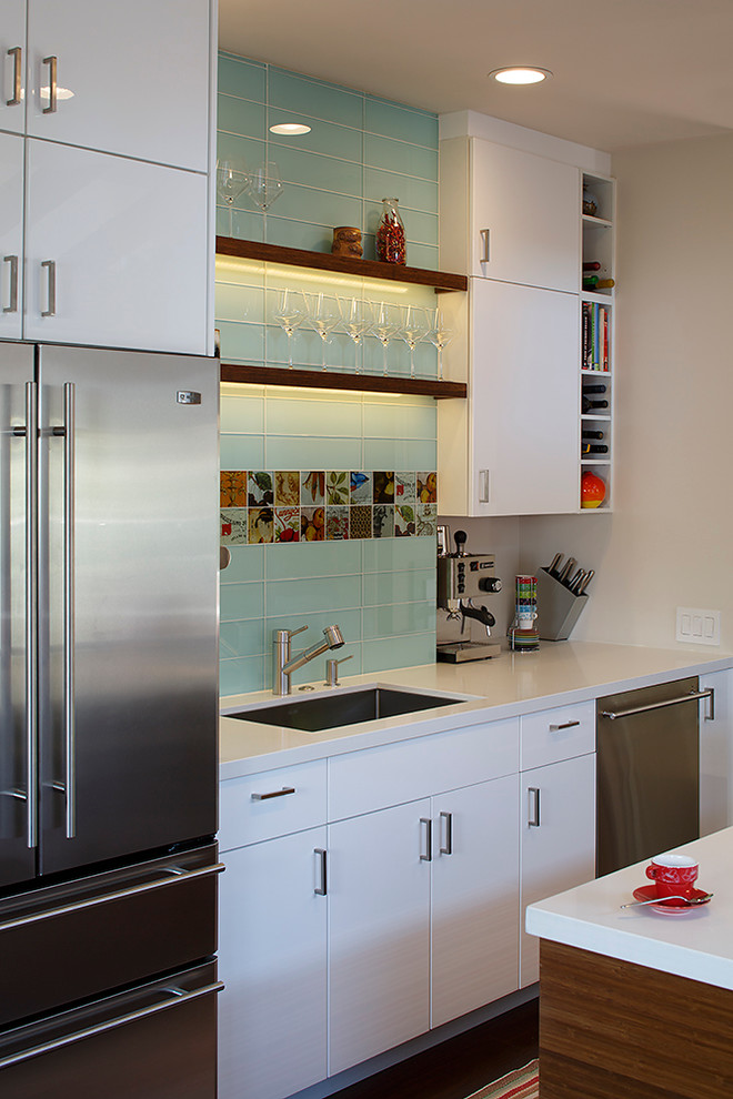 This is an example of a contemporary galley kitchen/diner in San Francisco with a submerged sink, flat-panel cabinets, white cabinets, blue splashback, glass tiled splashback and stainless steel appliances.