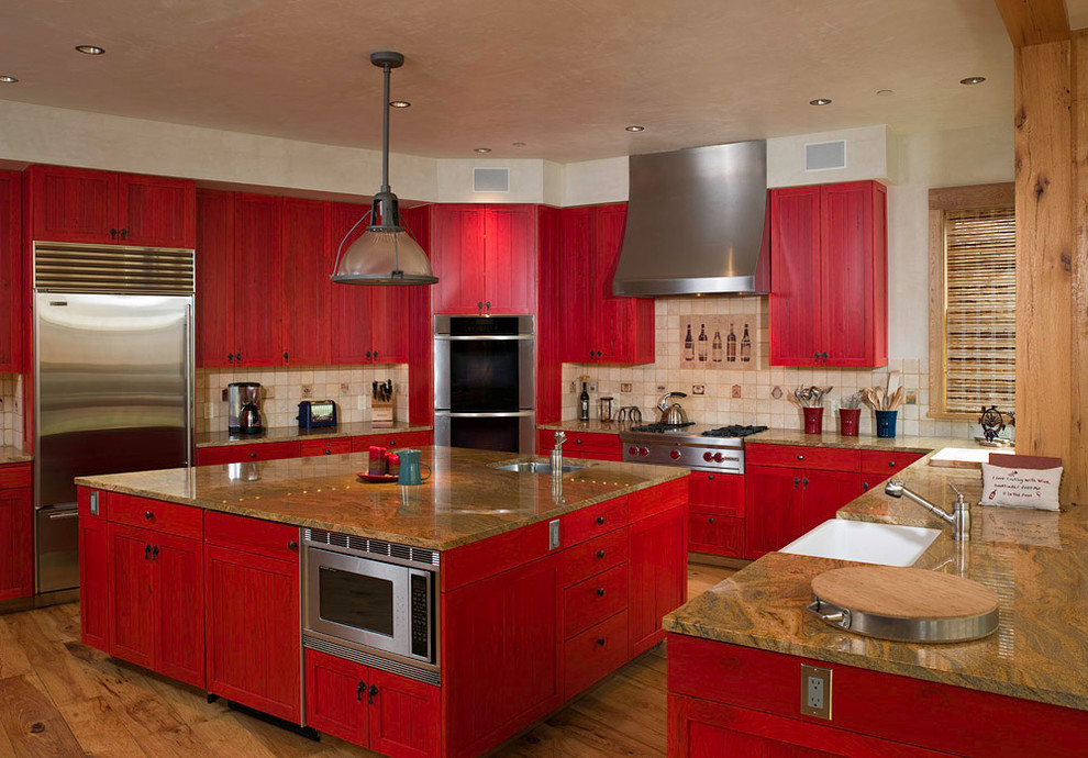 Große Rustikale Küche in U-Form mit Unterbauwaschbecken, Schrankfronten im Shaker-Stil, roten Schränken, Küchenrückwand in Beige, Küchengeräten aus Edelstahl, braunem Holzboden, Kücheninsel und Rückwand aus Steinfliesen in Denver
