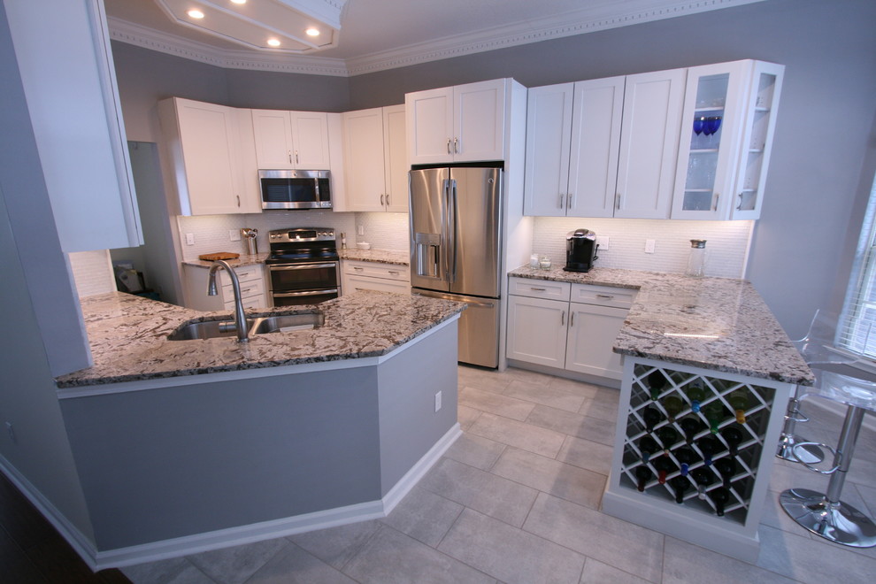 Trendy u-shaped porcelain tile eat-in kitchen photo in Jacksonville with shaker cabinets, white cabinets, granite countertops, glass tile backsplash, stainless steel appliances, a double-bowl sink, white backsplash and a peninsula