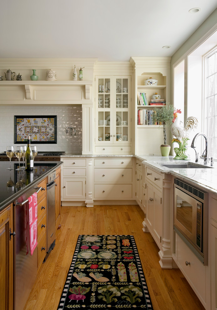 Klassische Wohnküche in L-Form mit Unterbauwaschbecken, flächenbündigen Schrankfronten, weißen Schränken, Küchengeräten aus Edelstahl, Küchenrückwand in Weiß und hellem Holzboden in Boston