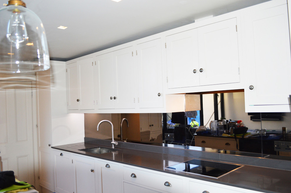 Bild på ett funkis linjärt kök och matrum, med släta luckor, vita skåp, marmorbänkskiva och glaspanel som stänkskydd