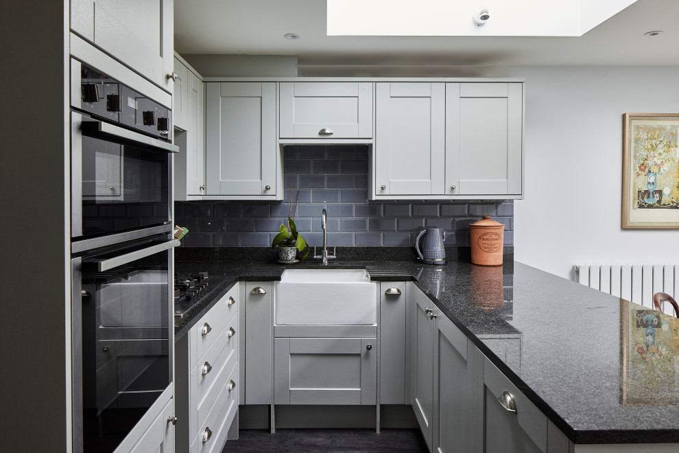 Mittelgroße Klassische Wohnküche in U-Form mit Landhausspüle, Schrankfronten im Shaker-Stil, grauen Schränken, Küchenrückwand in Grau, Rückwand aus Metrofliesen, grauem Boden und schwarzer Arbeitsplatte in London