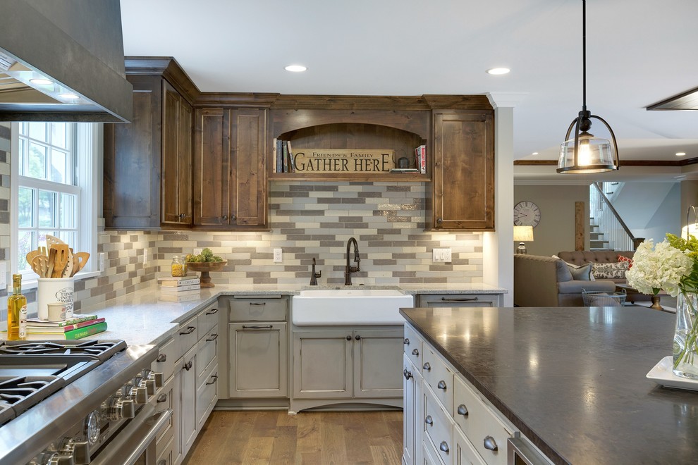 Photo of a large country u-shaped kitchen/diner in Minneapolis with a belfast sink, recessed-panel cabinets, grey cabinets, composite countertops, multi-coloured splashback, integrated appliances, an island, brown floors, porcelain splashback and medium hardwood flooring.