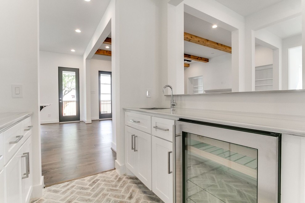 Inspiration for a transitional l-shaped brown floor open concept kitchen remodel in Houston with an undermount sink, shaker cabinets, white cabinets, gray backsplash, stainless steel appliances and an island