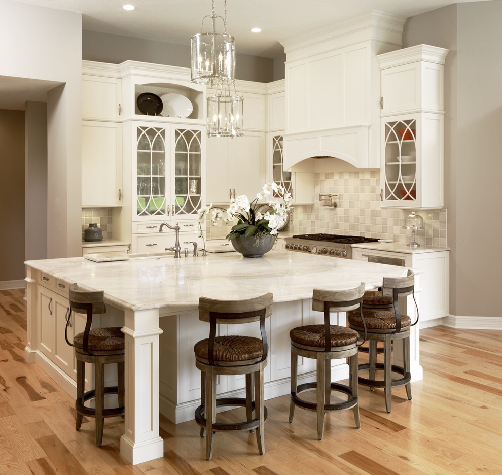 Inspiration for a mid-sized transitional l-shaped light wood floor open concept kitchen remodel in Tampa with a drop-in sink, glass-front cabinets, white cabinets, granite countertops, gray backsplash, ceramic backsplash, stainless steel appliances and an island