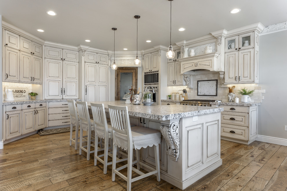 Foto på ett lantligt grå u-kök, med luckor med upphöjd panel, vita skåp, vitt stänkskydd, rostfria vitvaror, mörkt trägolv, en köksö och brunt golv