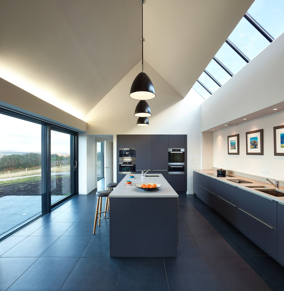 Contemporary u-shaped kitchen in Glasgow with a double-bowl sink, flat-panel cabinets, blue cabinets, black appliances, an island, black floors and grey worktops.