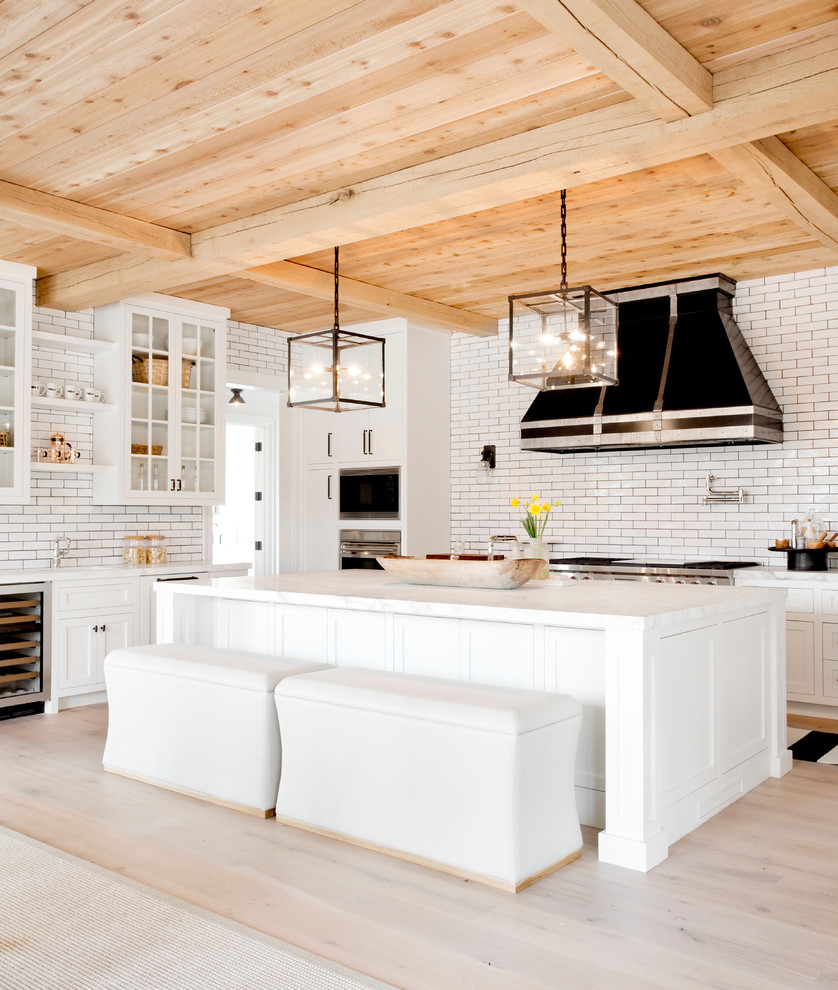 Huge transitional l-shaped light wood floor and beige floor kitchen photo in New York with shaker cabinets, white cabinets, white backsplash, subway tile backsplash, stainless steel appliances, an island, quartz countertops and a farmhouse sink