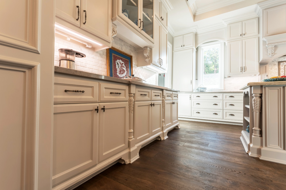 Inspiration for a large timeless u-shaped dark wood floor and brown floor eat-in kitchen remodel in Houston with a farmhouse sink, recessed-panel cabinets, white cabinets, quartzite countertops, white backsplash, marble backsplash, paneled appliances, two islands and gray countertops