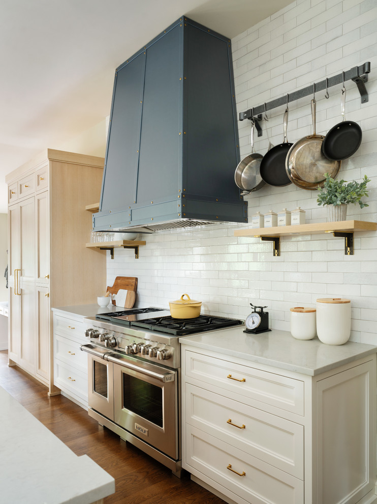 Klassisk inredning av ett stort vit vitt kök, med en rustik diskho, skåp i ljust trä, vitt stänkskydd, rostfria vitvaror, mellanmörkt trägolv, en köksö och luckor med infälld panel