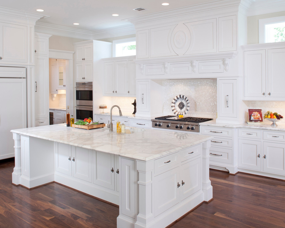 Inredning av ett klassiskt kök, med marmorbänkskiva, luckor med profilerade fronter, vita skåp, vitt stänkskydd, stänkskydd i mosaik och integrerade vitvaror