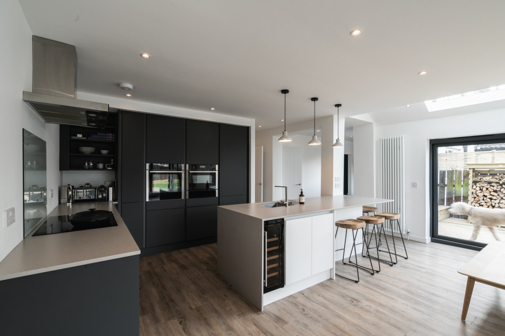Inspiration for a contemporary l-shaped kitchen in Glasgow with a submerged sink, flat-panel cabinets, black cabinets, black appliances, medium hardwood flooring, an island, brown floors and grey worktops.