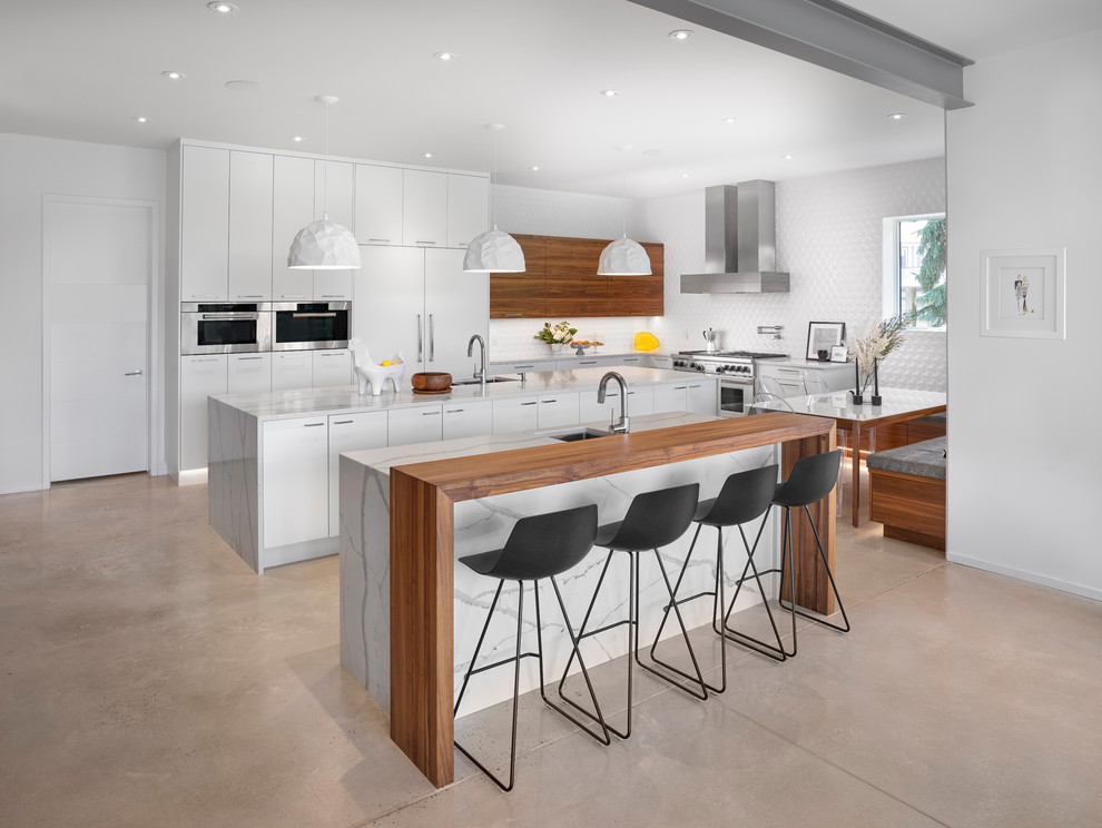 Example of a trendy l-shaped concrete floor and beige floor kitchen design in Edmonton with an undermount sink, flat-panel cabinets, white cabinets, white backsplash, paneled appliances, two islands and white countertops