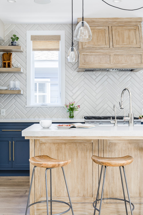 The cabinets have white herringbone backsplash tile, which is a nice contrast to the blue cabinets. The tile is a great way to add some color and pattern to this kitchen without being too busy.