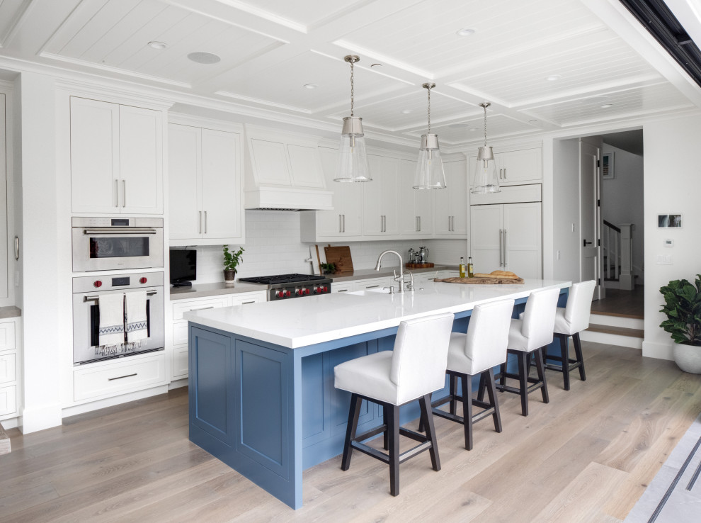 Inspiration for a coastal l-shaped medium tone wood floor and brown floor kitchen remodel in Orange County with shaker cabinets, white cabinets, stainless steel appliances, an island and white countertops
