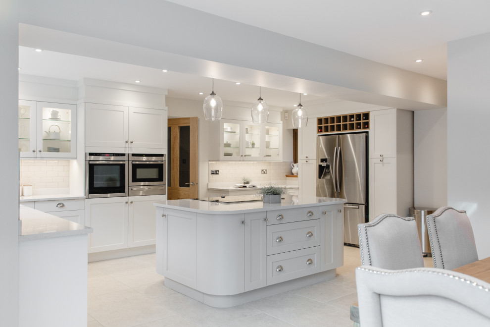 This is an example of a traditional u-shaped kitchen in Other with shaker cabinets, white cabinets, white splashback, metro tiled splashback, stainless steel appliances, an island, grey floors and white worktops.