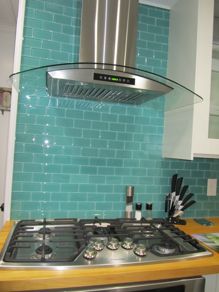 Example of a small minimalist galley porcelain tile kitchen design in Other with glass-front cabinets, white cabinets, wood countertops, blue backsplash, glass tile backsplash and stainless steel appliances