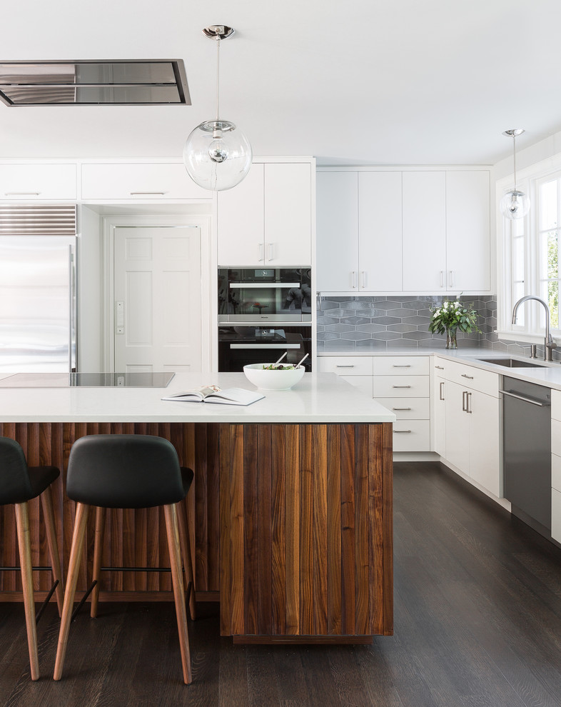 This is an example of a classic l-shaped kitchen in Portland with a submerged sink, flat-panel cabinets, white cabinets, grey splashback, dark hardwood flooring, an island and brown floors.