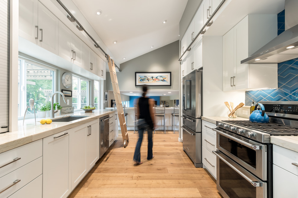 Eat-in kitchen - mid-sized transitional galley medium tone wood floor eat-in kitchen idea in San Diego with an undermount sink, shaker cabinets, white cabinets, quartzite countertops, blue backsplash, porcelain backsplash, stainless steel appliances and no island