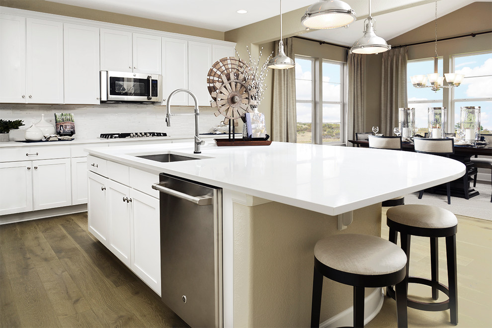 Modelo de cocina contemporánea con puertas de armario blancas, salpicadero blanco, electrodomésticos de acero inoxidable, una isla y encimeras blancas