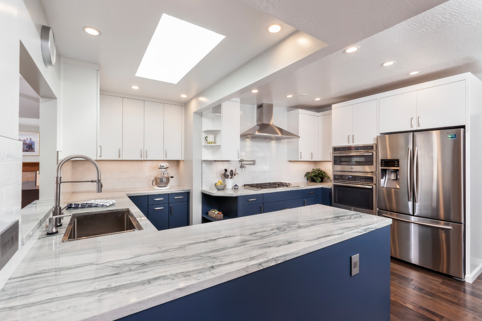 Inspiration for a contemporary u-shaped kitchen/diner in San Francisco with blue cabinets, white splashback, metro tiled splashback, stainless steel appliances, no island, a built-in sink, flat-panel cabinets, medium hardwood flooring, brown floors and grey worktops.