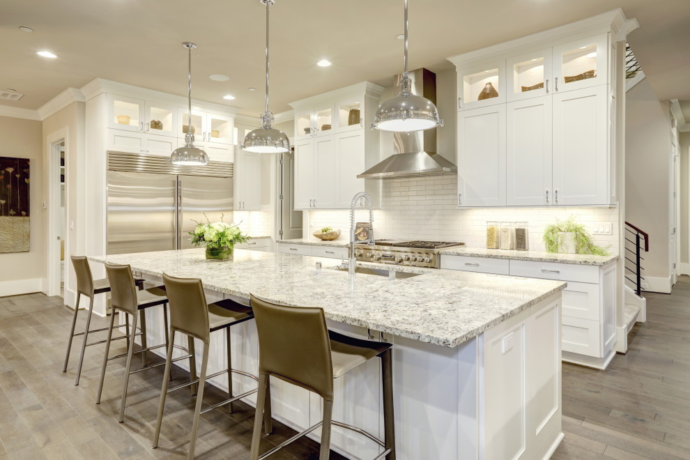 Foto på ett stort amerikanskt vit kök, med en undermonterad diskho, luckor med upphöjd panel, vita skåp, marmorbänkskiva, vitt stänkskydd, stänkskydd i keramik, rostfria vitvaror, klinkergolv i keramik, en köksö och grått golv