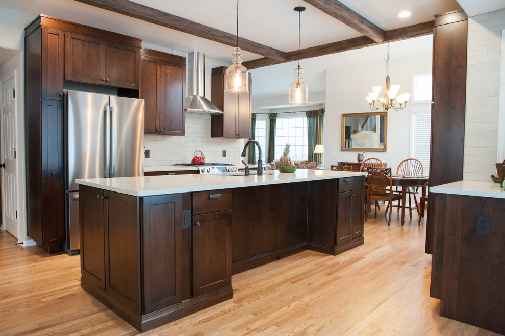 Inspiration for a large transitional galley light wood floor and yellow floor eat-in kitchen remodel in Denver with a single-bowl sink, shaker cabinets, medium tone wood cabinets, quartz countertops, beige backsplash, porcelain backsplash, stainless steel appliances, an island and white countertops