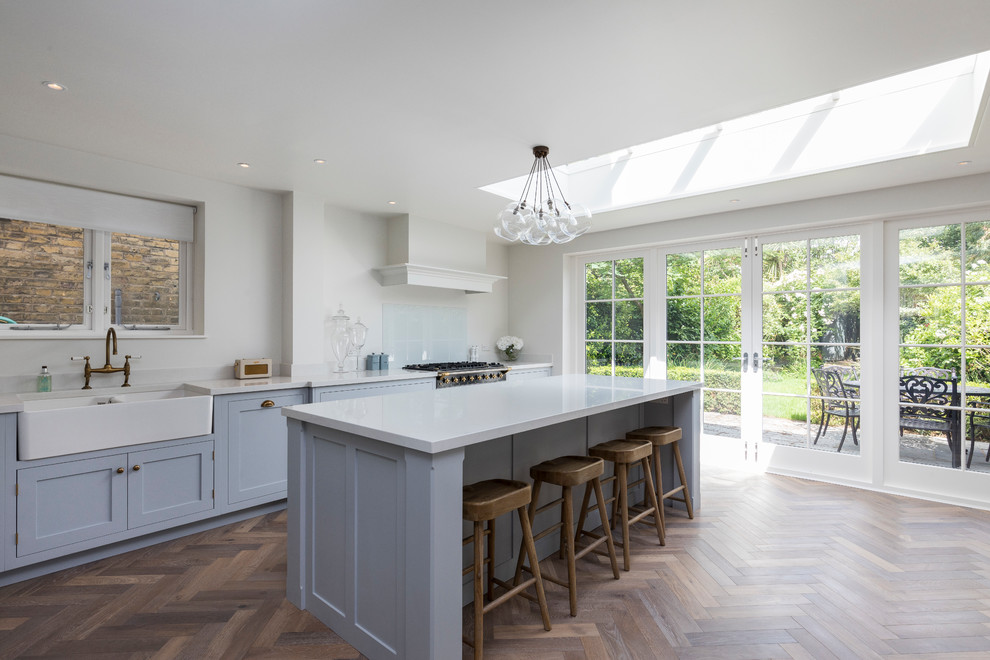 Inspiration for a medium sized traditional l-shaped kitchen/diner in London with a belfast sink, shaker cabinets, blue cabinets, stainless steel appliances, medium hardwood flooring, a breakfast bar and brown floors.