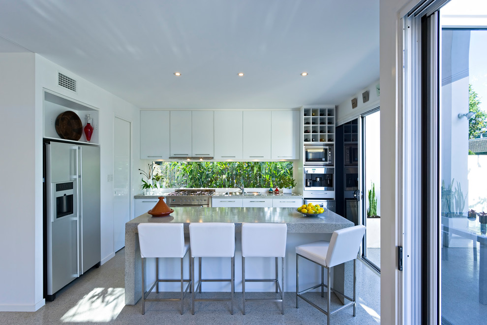 Modern inredning av ett mellanstort kök, med släta luckor, vita skåp, rostfria vitvaror, en köksö och terrazzogolv