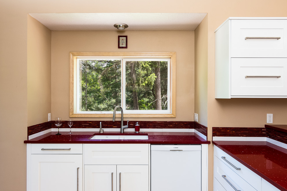 ポートランドにあるお手頃価格の中くらいなトラディショナルスタイルのおしゃれなキッチン (アンダーカウンターシンク、シェーカースタイル扉のキャビネット、白いキャビネット、クオーツストーンカウンター、赤いキッチンパネル、ガラス板のキッチンパネル、シルバーの調理設備、淡色無垢フローリング、茶色い床、赤いキッチンカウンター、窓) の写真
