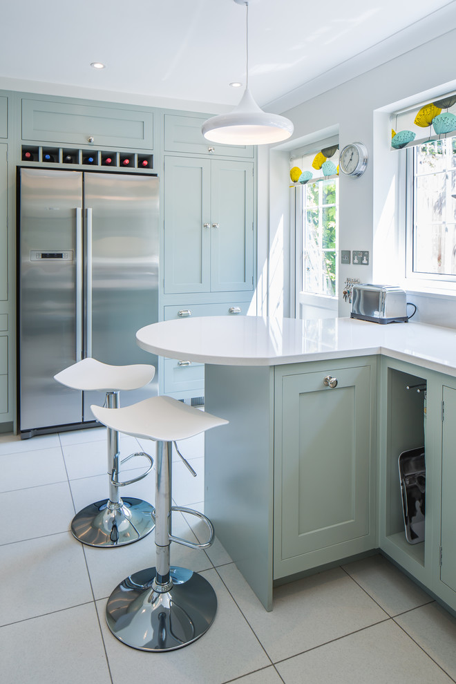 Photo of a medium sized contemporary u-shaped kitchen/diner in Oxfordshire with a built-in sink, shaker cabinets, turquoise cabinets, laminate countertops, white splashback, glass sheet splashback, stainless steel appliances, slate flooring, a breakfast bar and white floors.