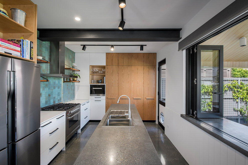 Industriell inredning av ett avskilt, mellanstort kök, med en dubbel diskho, grönt stänkskydd, rostfria vitvaror, betonggolv, en köksö och grått golv