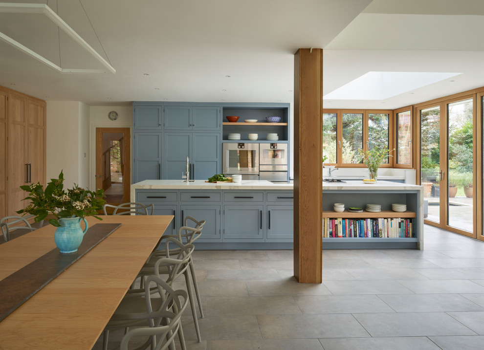 Свежая идея для дизайна: параллельная кухня в стиле неоклассика (современная классика) с фасадами в стиле шейкер, синими фасадами, техникой из нержавеющей стали, островом, серым полом и белой столешницей - отличное фото интерьера