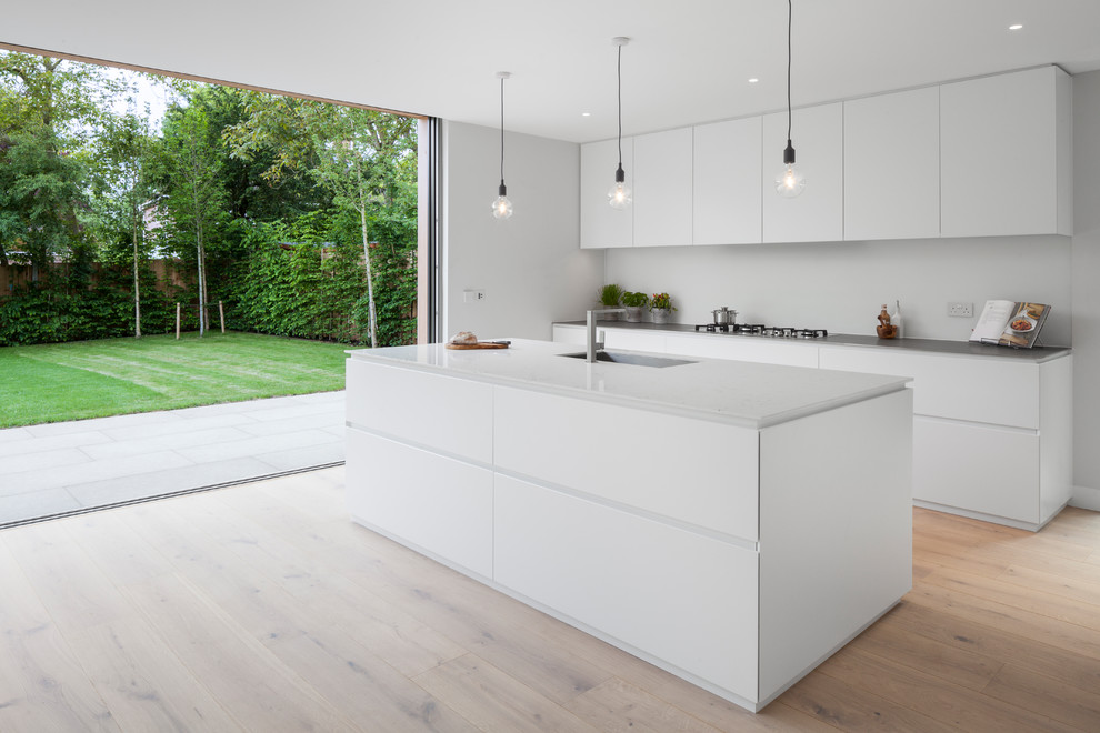 Immagine di una cucina minimalista con lavello sottopiano, ante lisce, ante bianche, top in acciaio inossidabile, paraspruzzi bianco, paraspruzzi con lastra di vetro, parquet chiaro e pavimento marrone