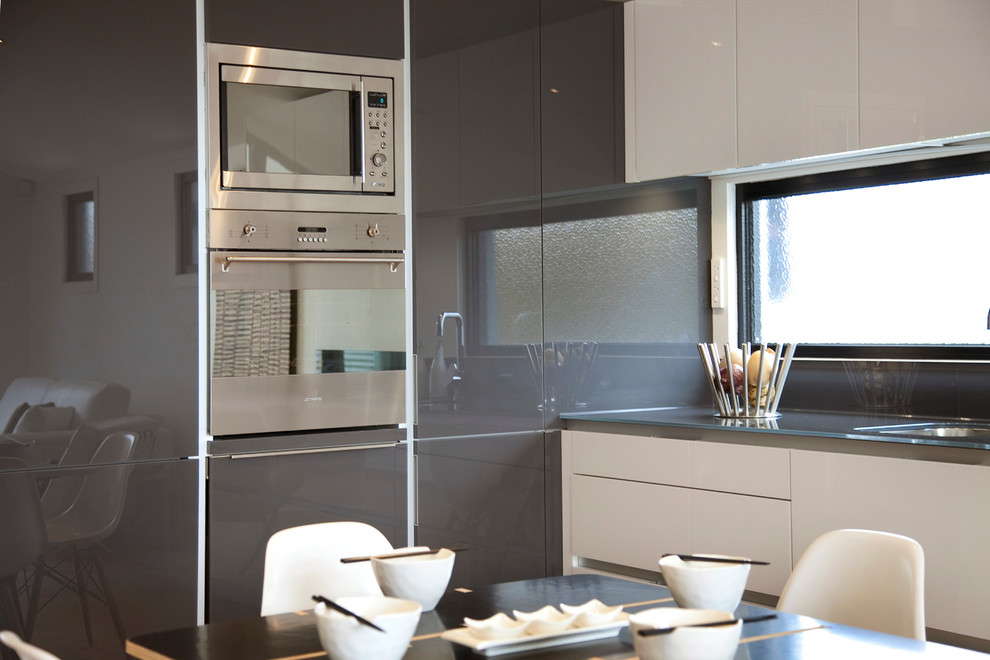 Modern inredning av ett l-kök, med en integrerad diskho, luckor med glaspanel, vita skåp, bänkskiva i glas och rostfria vitvaror