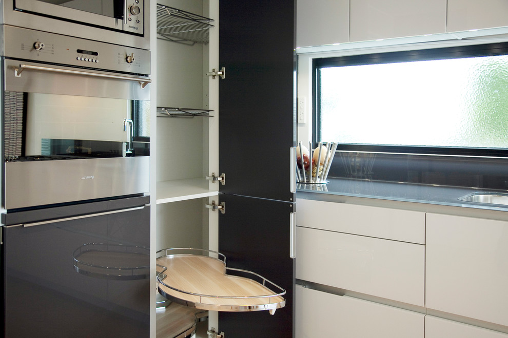 Idéer för ett modernt l-kök, med en integrerad diskho, luckor med glaspanel, vita skåp, bänkskiva i glas och rostfria vitvaror
