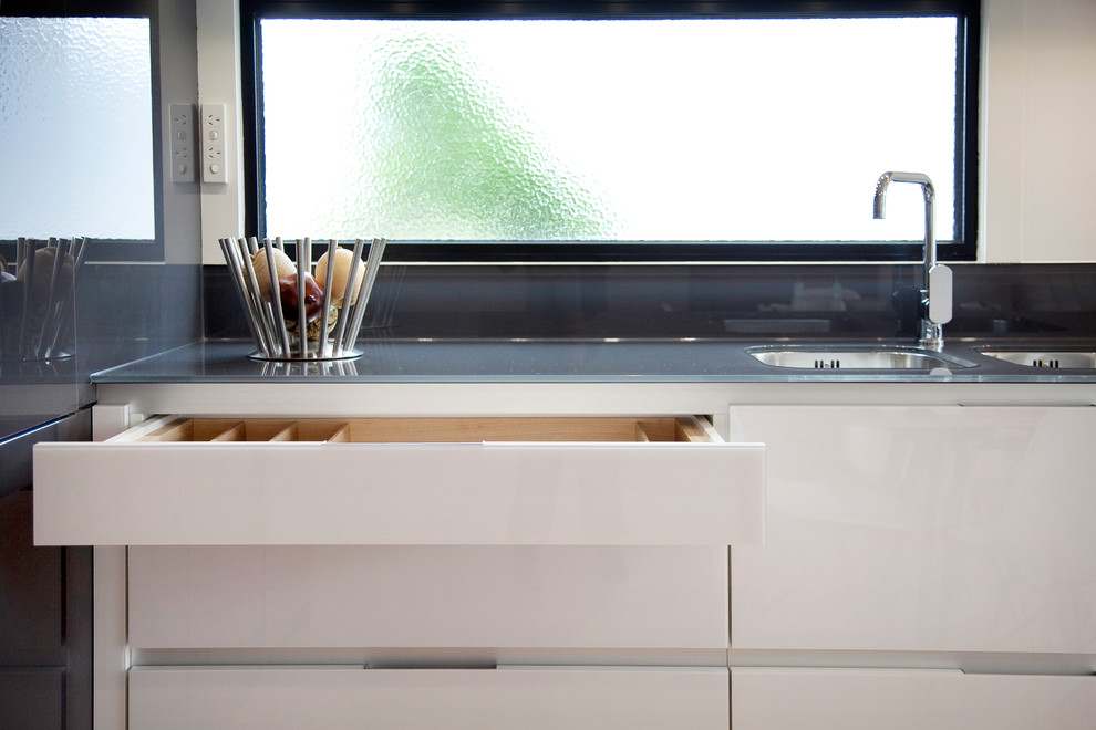 Ejemplo de cocinas en L actual con fregadero integrado, armarios tipo vitrina, puertas de armario blancas, encimera de vidrio y electrodomésticos de acero inoxidable