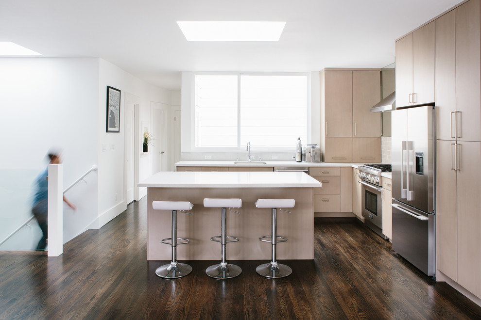 Large eclectic l-shaped dark wood floor kitchen photo in San Francisco with a drop-in sink, flat-panel cabinets, light wood cabinets, solid surface countertops, white backsplash, subway tile backsplash, stainless steel appliances and an island