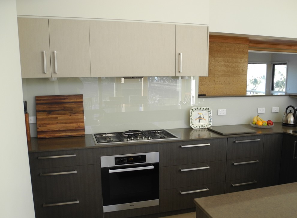 This is an example of a medium sized contemporary u-shaped open plan kitchen in Melbourne with a double-bowl sink, flat-panel cabinets, engineered stone countertops, glass sheet splashback, stainless steel appliances, porcelain flooring, dark wood cabinets, white splashback and an island.