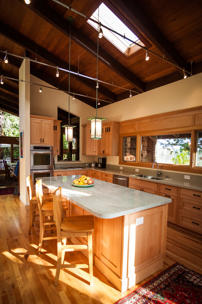 Foto på ett avskilt, mellanstort amerikanskt l-kök, med en dubbel diskho, skåp i shakerstil, skåp i ljust trä, bänkskiva i kvartsit, grönt stänkskydd, stänkskydd i sten, rostfria vitvaror, mellanmörkt trägolv och en köksö
