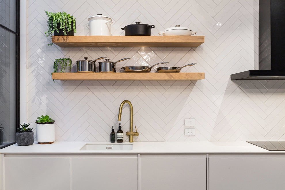 Modern inredning av ett mellanstort vit vitt kök, med en undermonterad diskho, släta luckor, vita skåp, marmorbänkskiva, vitt stänkskydd, stänkskydd i mosaik, svarta vitvaror, betonggolv, en köksö och grått golv