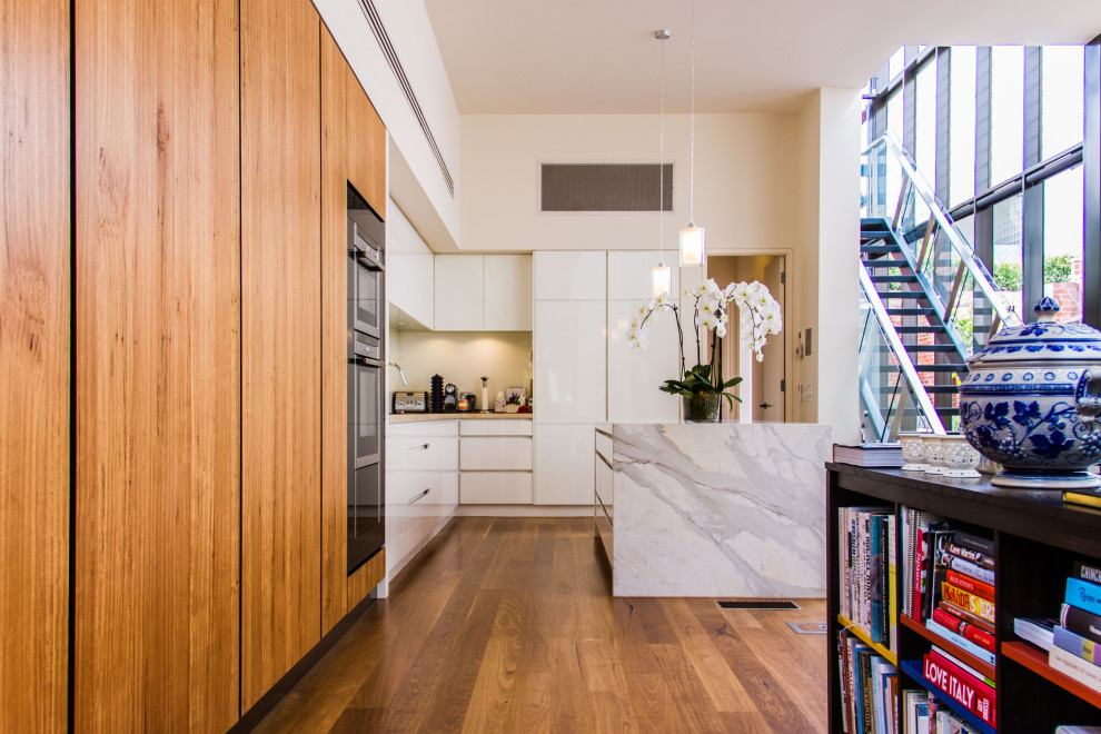 Moderne Küche in L-Form mit flächenbündigen Schrankfronten, weißen Schränken, Küchengeräten aus Edelstahl, braunem Holzboden, Kücheninsel, braunem Boden und grauer Arbeitsplatte in Melbourne