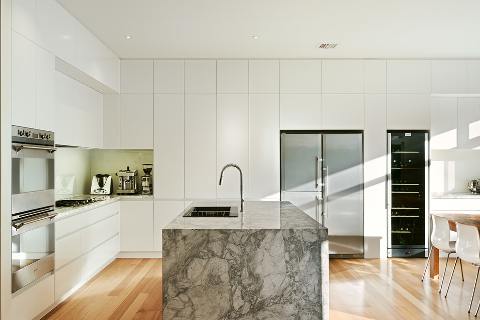Moderne Küche in L-Form mit Doppelwaschbecken, weißen Schränken, Küchengeräten aus Edelstahl, Kücheninsel, flächenbündigen Schrankfronten und braunem Holzboden in Melbourne