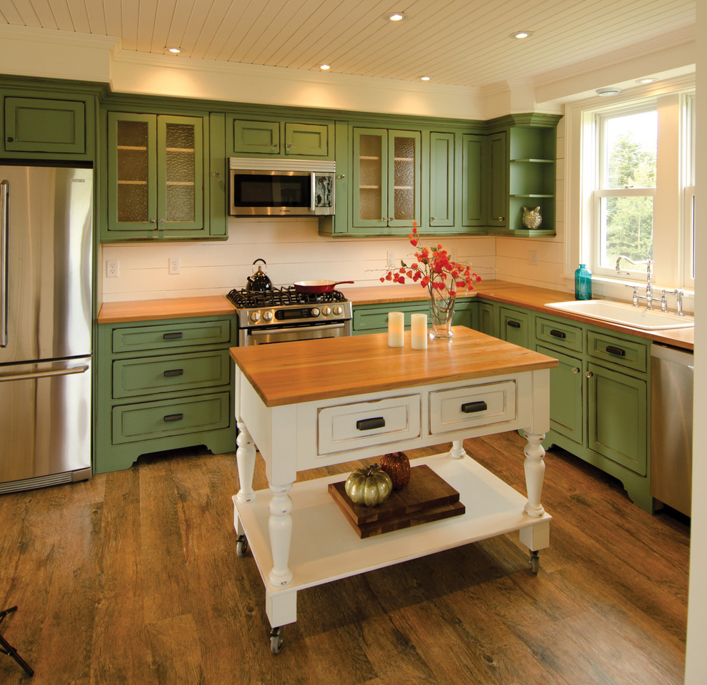 Klassisk inredning av ett kök, med en nedsänkt diskho, luckor med profilerade fronter, gröna skåp, träbänkskiva och rostfria vitvaror