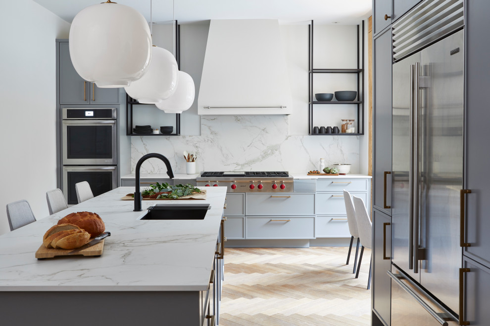 Modern inredning av ett stort vit vitt l-kök, med en undermonterad diskho, grå skåp, vitt stänkskydd, stänkskydd i sten, rostfria vitvaror, en köksö, släta luckor, ljust trägolv och beiget golv