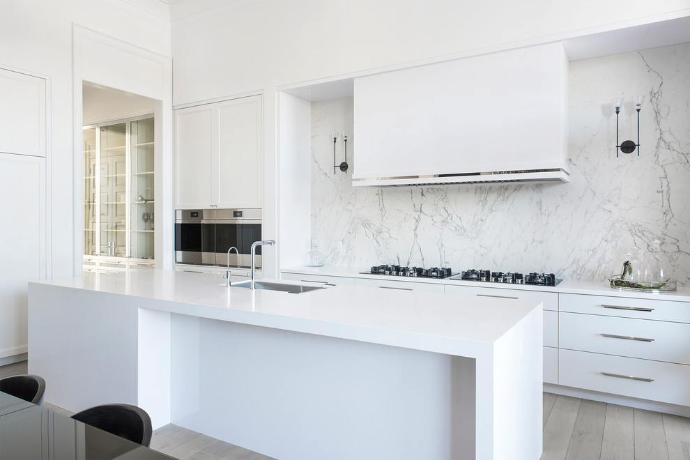 Foto på ett funkis vit kök och matrum, med en undermonterad diskho, släta luckor, vitt stänkskydd, stänkskydd i sten, rostfria vitvaror, ljust trägolv, en köksö och beiget golv