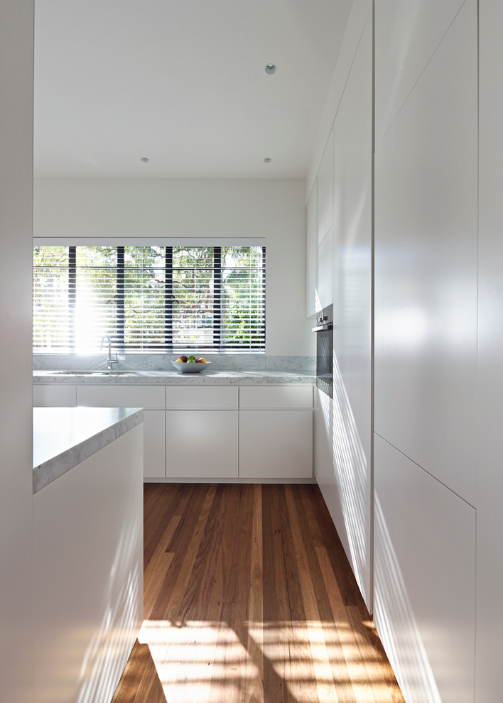This is an example of a medium sized contemporary u-shaped enclosed kitchen in Sydney with a submerged sink, flat-panel cabinets, white cabinets, marble worktops, stainless steel appliances and medium hardwood flooring.