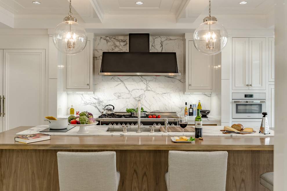 Inredning av ett klassiskt stort kök, med en undermonterad diskho, luckor med infälld panel, vita skåp, marmorbänkskiva, grått stänkskydd, stänkskydd i marmor, integrerade vitvaror, ljust trägolv, en köksö och beiget golv